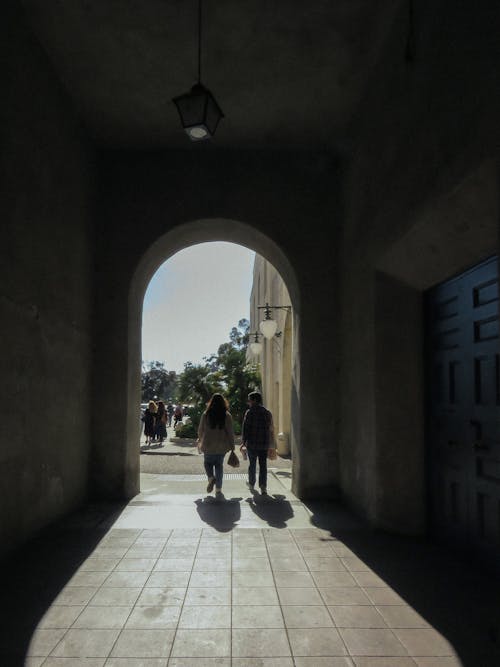 Two people walking through an archway in the sun