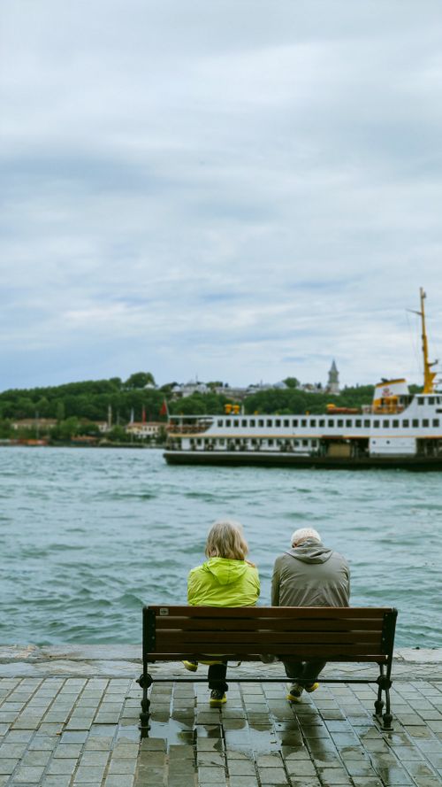 Free A couple sits on a bench by the Bosphorus in Istanbul, with a ferry passing by. Stock Photo