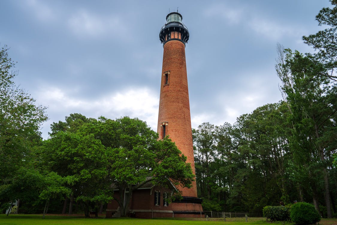 A tall brick lighthouse with a green grassy area