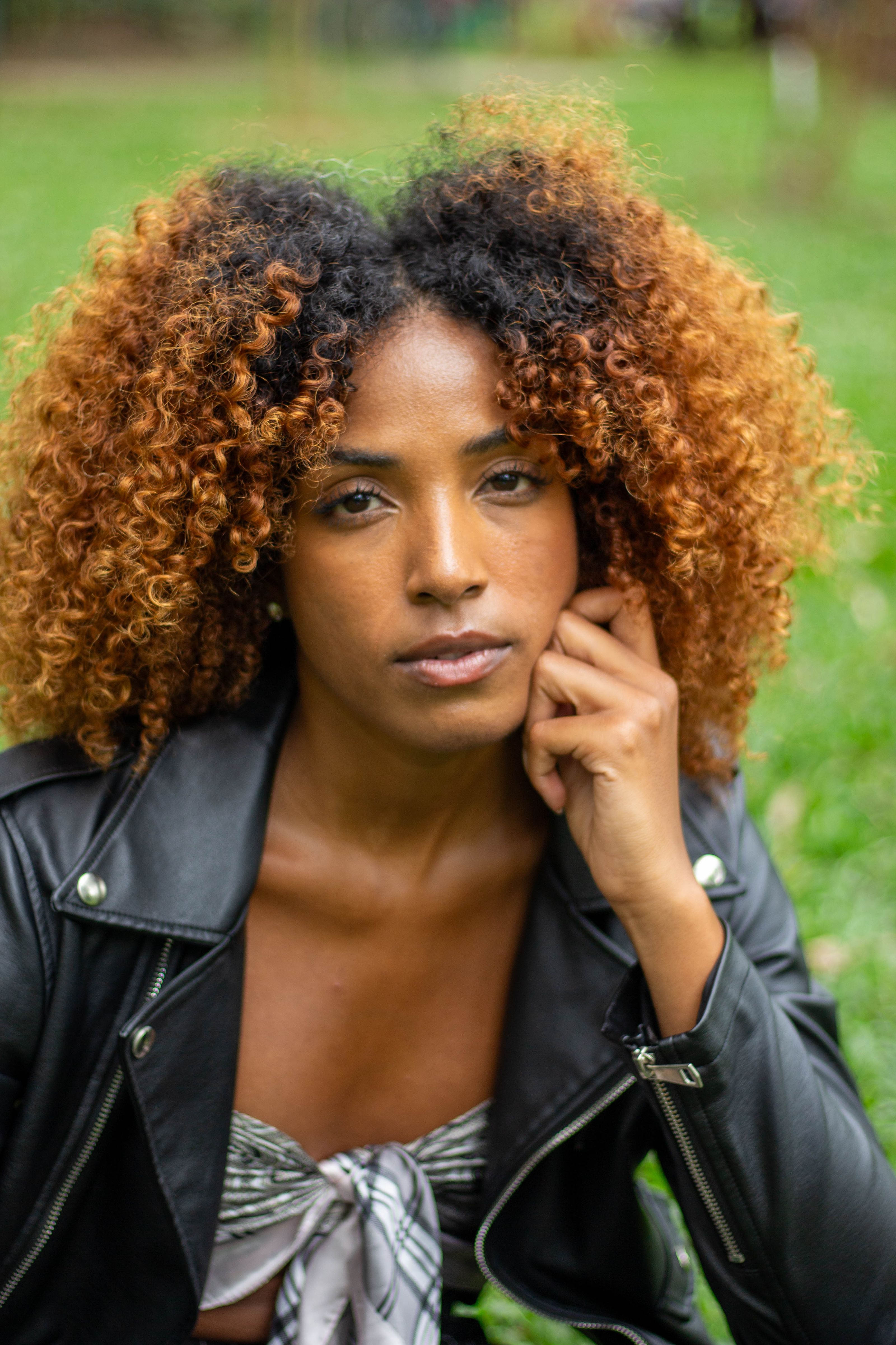 Mulher fashion com cabelo cacheado posa com uma jaqueta de couro preta ao ar livre.