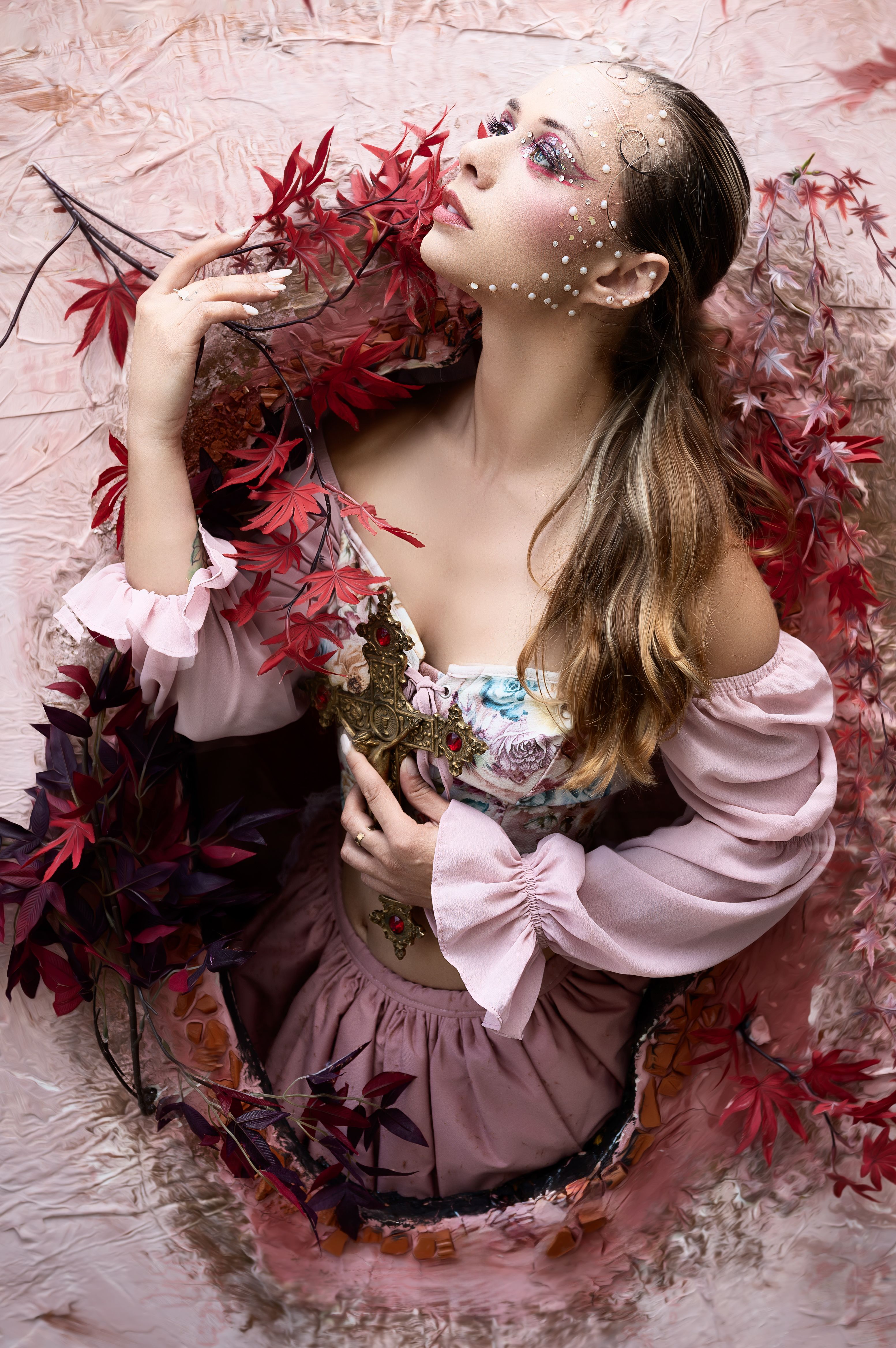 Artistic portrait of a woman with makeup and long hair, surrounded by vibrant red leaves.