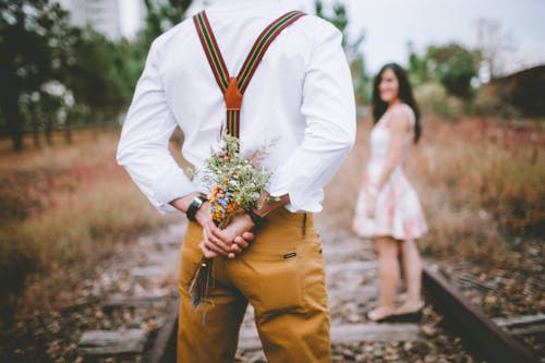 Free Man Holding Flowers Standing Beside Woman on Railroad Stock Photo