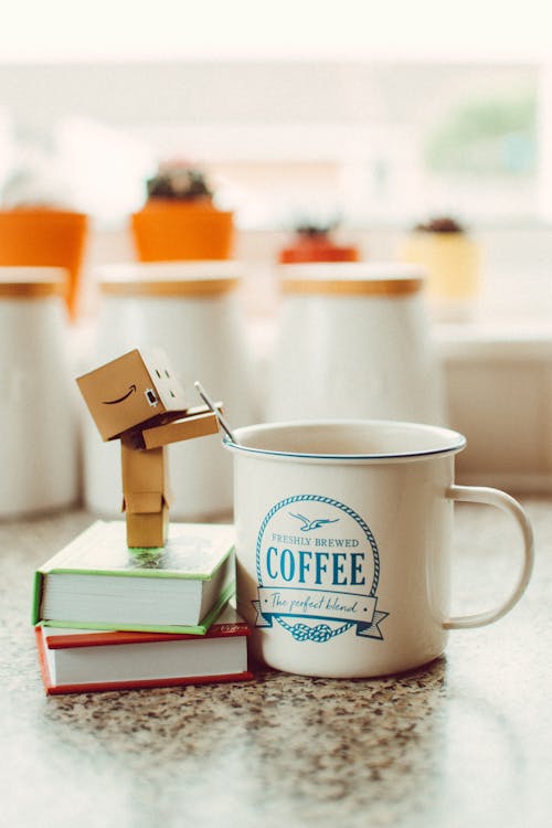 Free Cartoon Robot Standing on Books Beside Mug Stock Photo