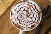 木桌上的卡布奇诺特写中，泡沫上绘有复杂的巧克力图案