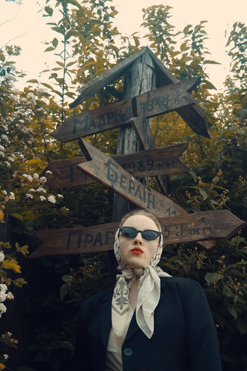 A woman in a suit and sunglasses standing next to a wooden sign