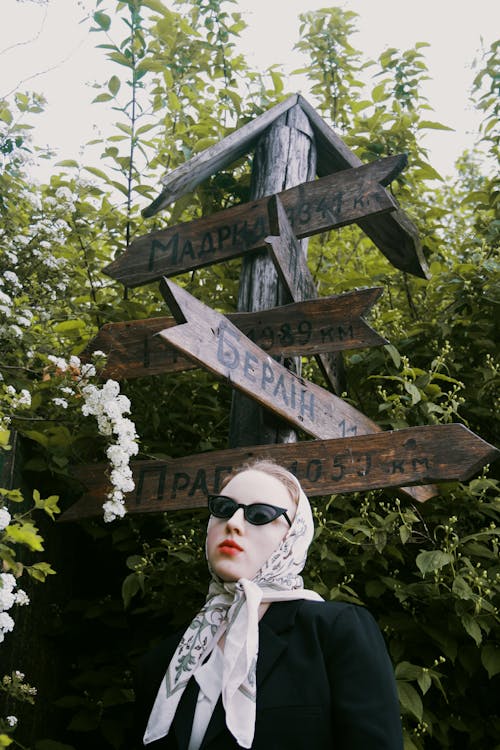 A woman in sunglasses and a scarf posing in front of a sign