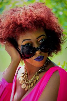 Vibrant portrait of a fashionable woman with curly hair, bold makeup, and sunglasses, showcasing modern style.