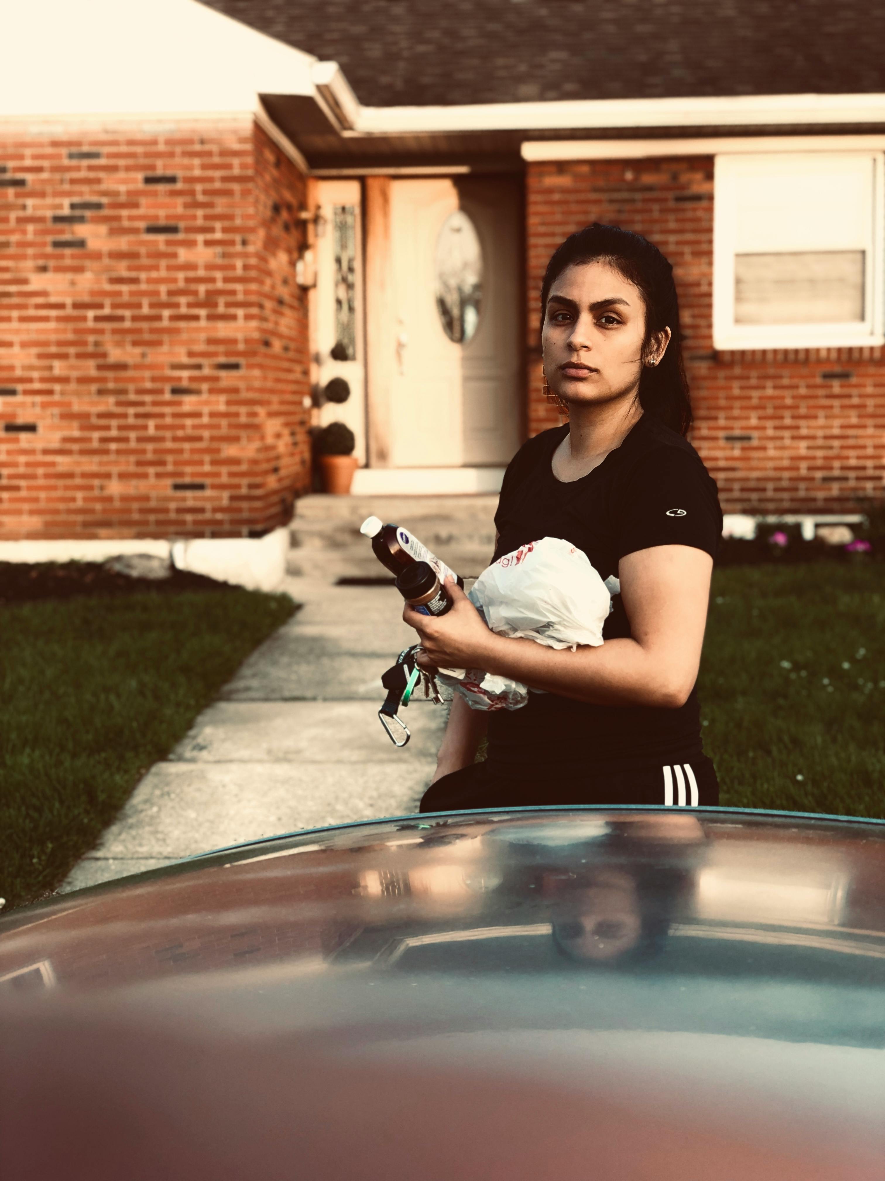 一名妇女手持物品，站在宾夕法尼亚州阿伦敦的一栋砖房外，描绘着日常生活