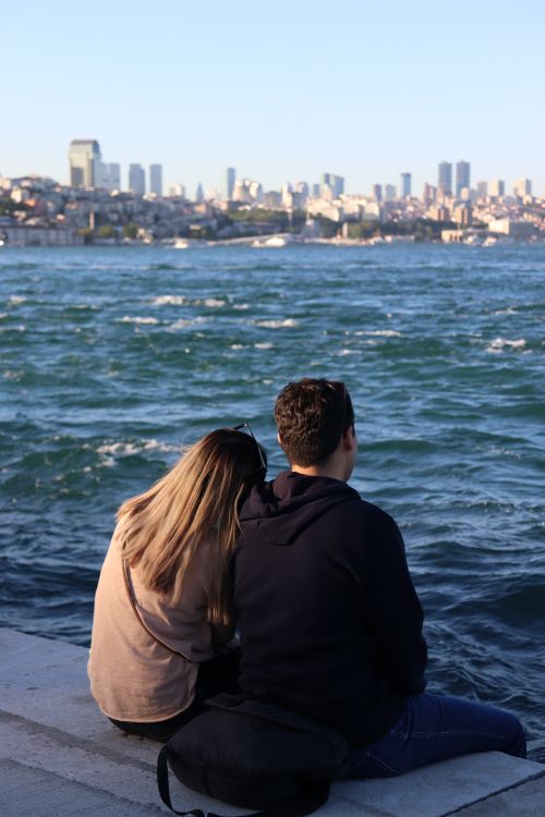 Free Couple sitting by the Bosphorus with an Istanbul skyline backdrop on a clear day. Stock Photo