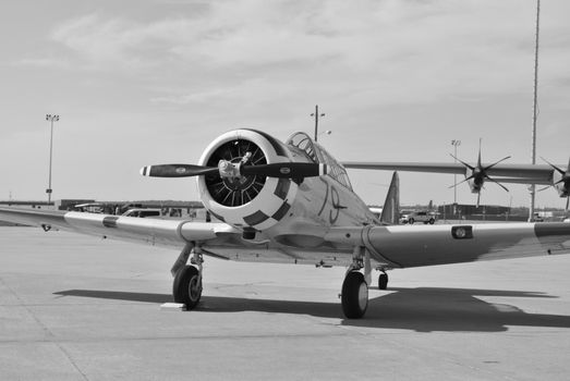 Black and white photo of a vintage propeller plane parked on an airport tarmac under a clear sky.