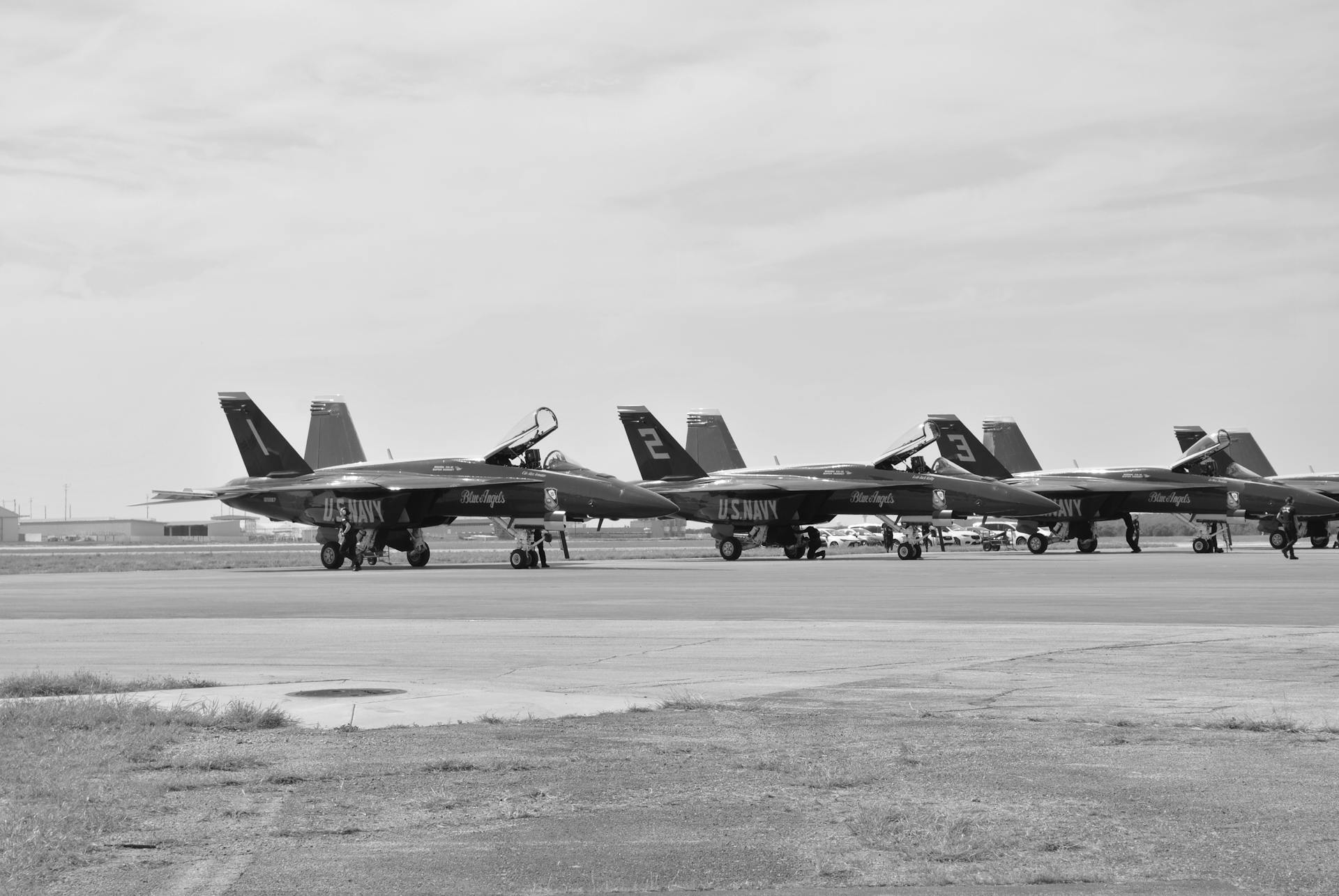 Monochrome image of US Navy Blue Angels jets parked on an airport runway.