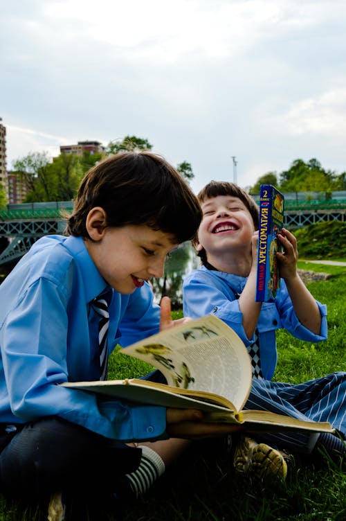Bezpłatne Dwóch Chłopców Siedzących Na Trawie, śmiejących Się I Czytających Książki Zdjęcie z galerii