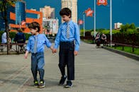 两个穿着蓝色衬衫的小男孩手牵着手走在城市的人行道上