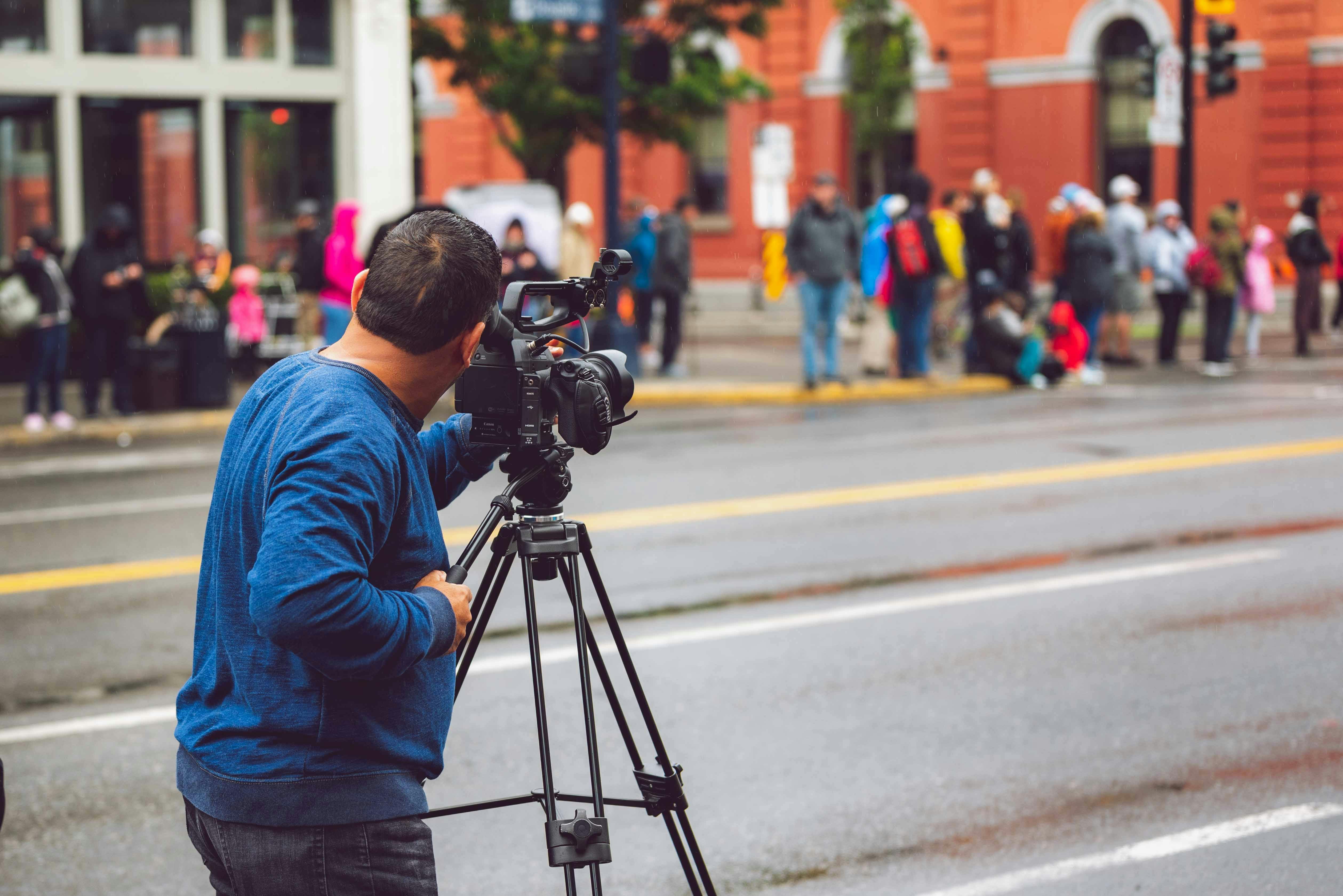 camera man with video camera on tripod position by the street across people at the sidewalk