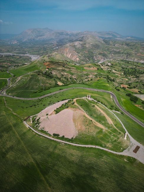 Aerial shot of a winding road through lush, green mountains and valleys.