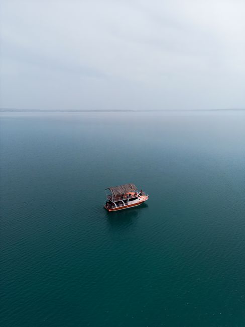 A solitary boat sails calmly across a vast, foggy lake, showcasing serene travel and nature vibes.