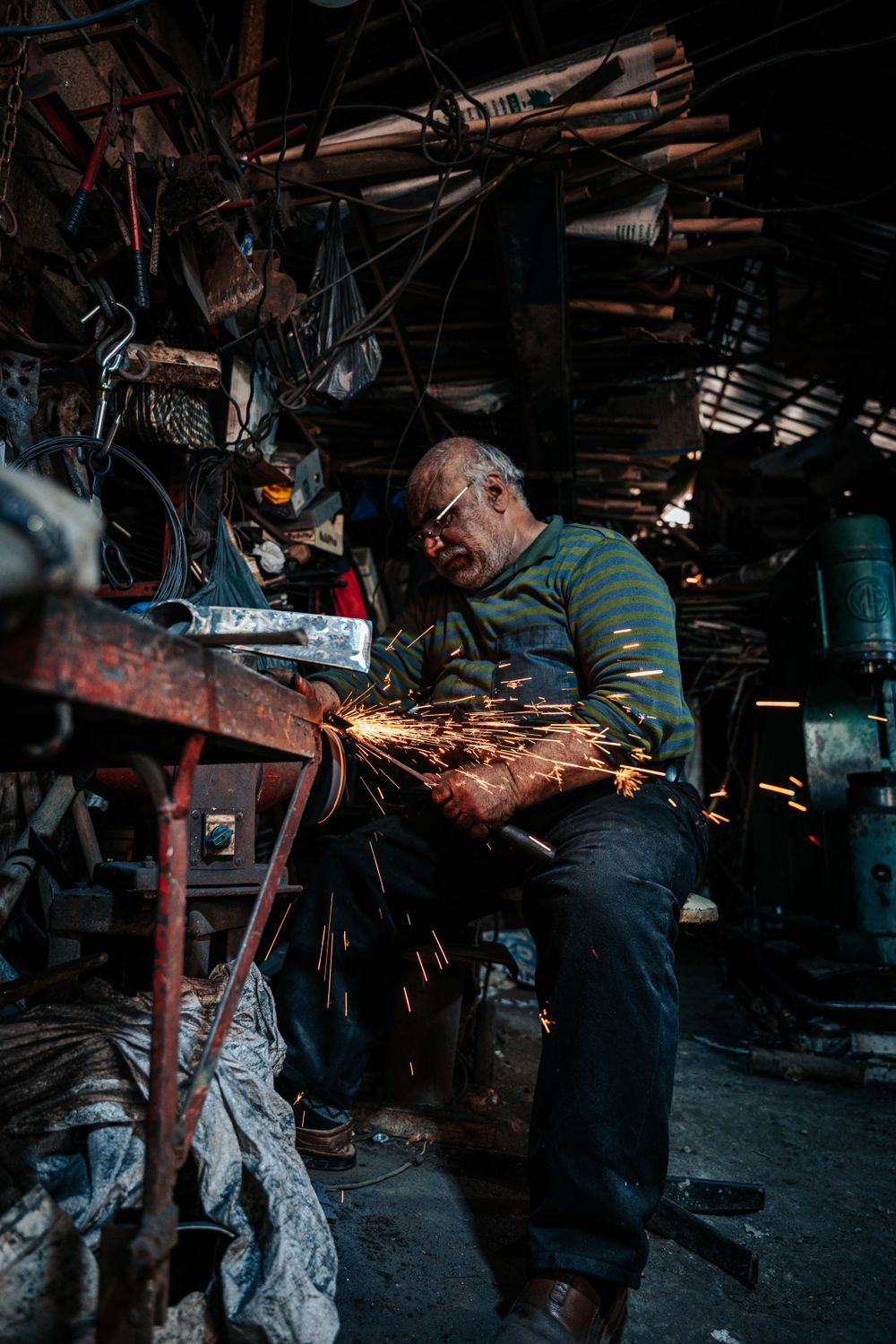 Metalworker grinding a bell rim in a cluttered workshop, sparks flying — photo by Yunus Tuğ on Pexels