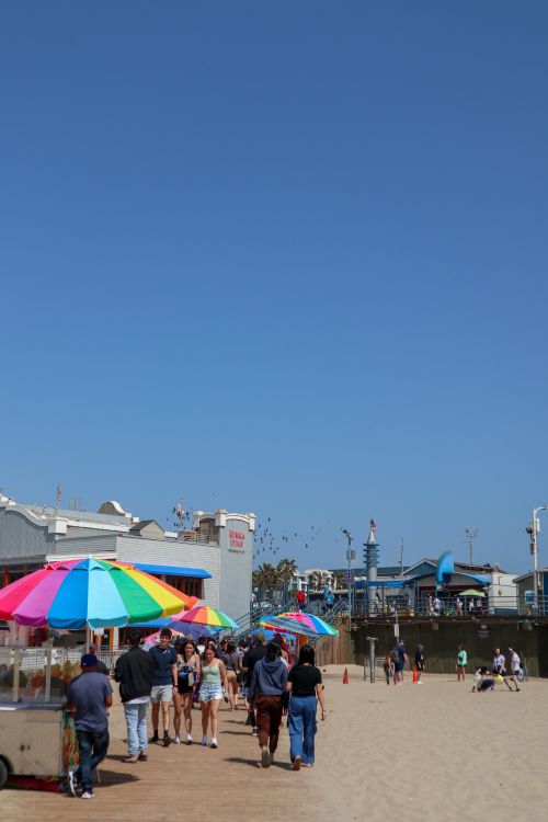 Free A colorful beach scene at Santa Monica with people, umbrellas, and an ice cream cart. Stock Photo