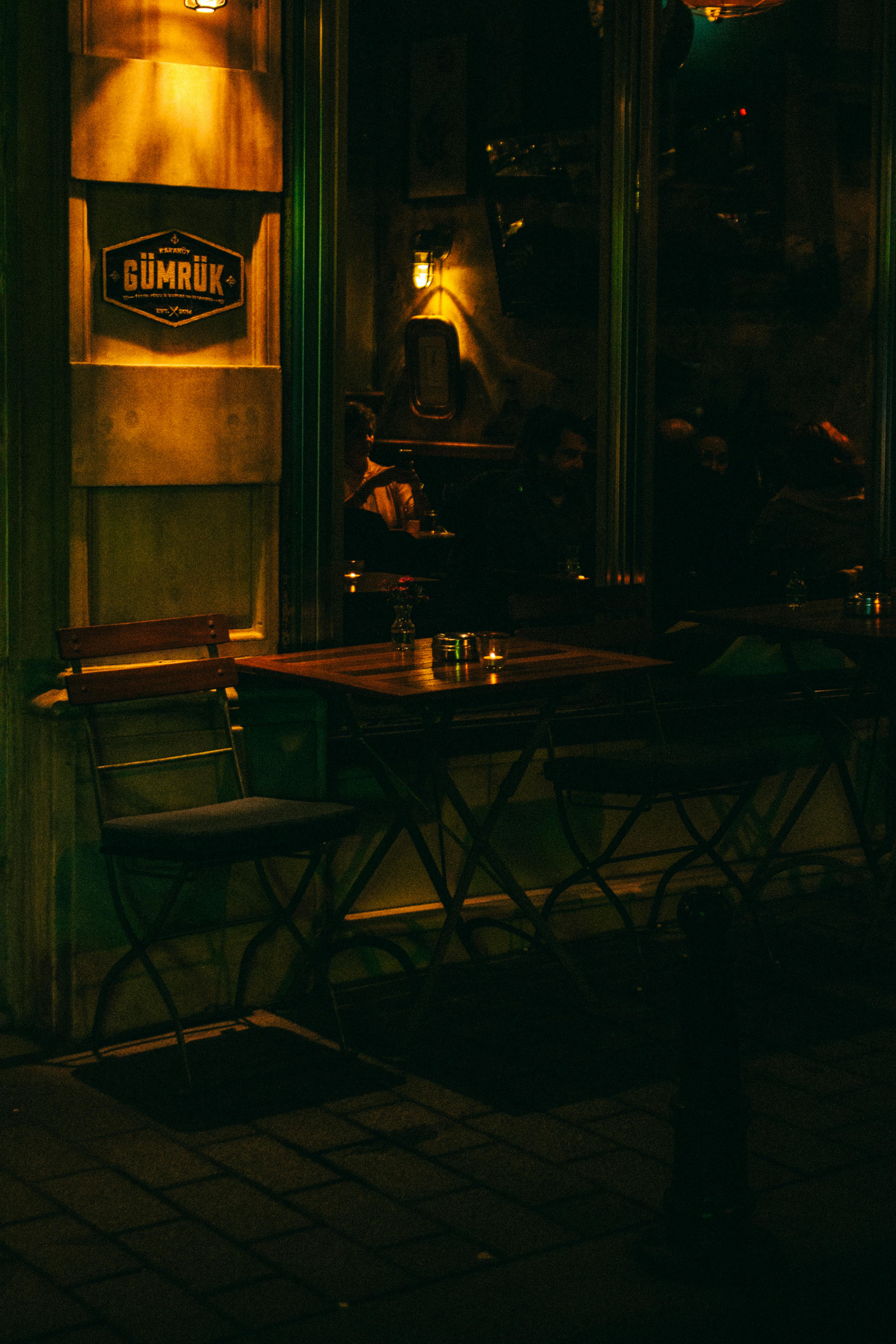 Warmly lit outdoor café scene at night with empty tables and reflections.