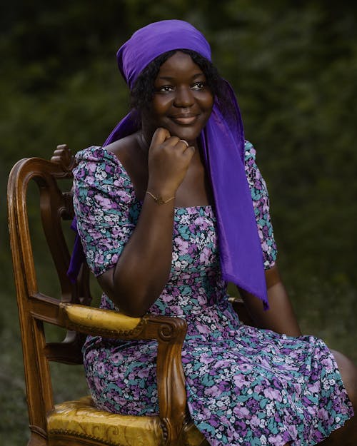 A woman in purple dress and purple headscarf sitting on a chair