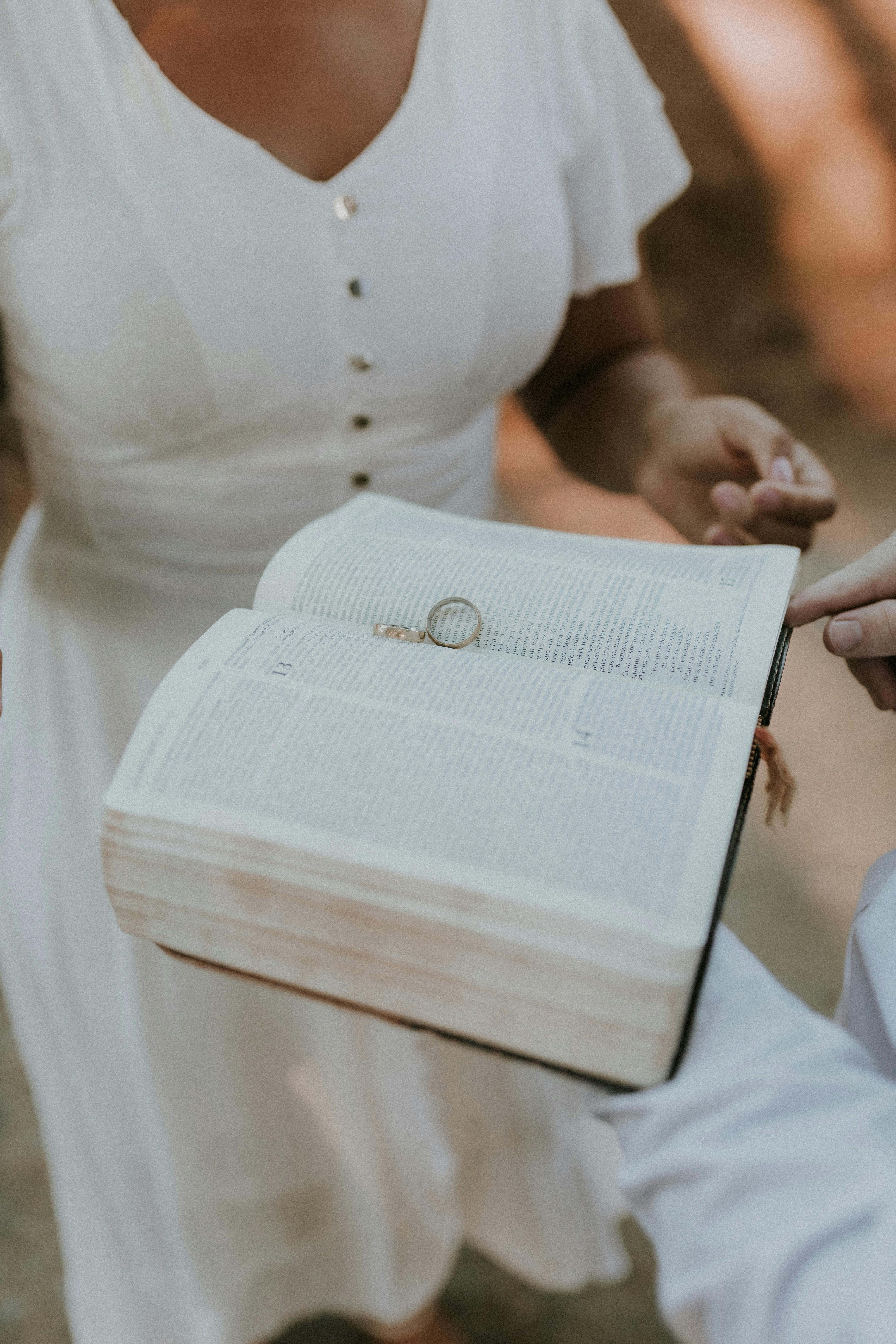 A couple holds a Bible with wedding rings inside, symbolizing love and commitment.