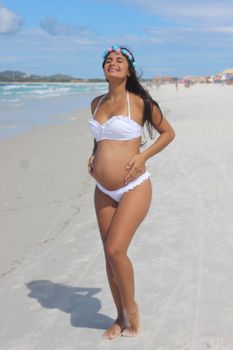Expectant mother enjoys the sun on a sandy tropical beach, radiating happiness.