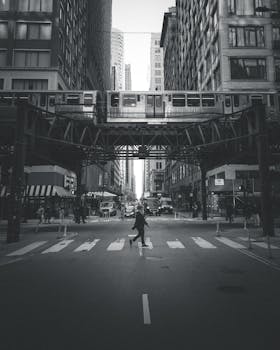 Black and white photo of a busy Chicago street with an elevated train and pedestrians crossing.
