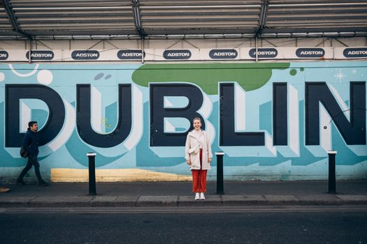 Woman poses in front of colorful Dublin wall mural with passersby on city street.