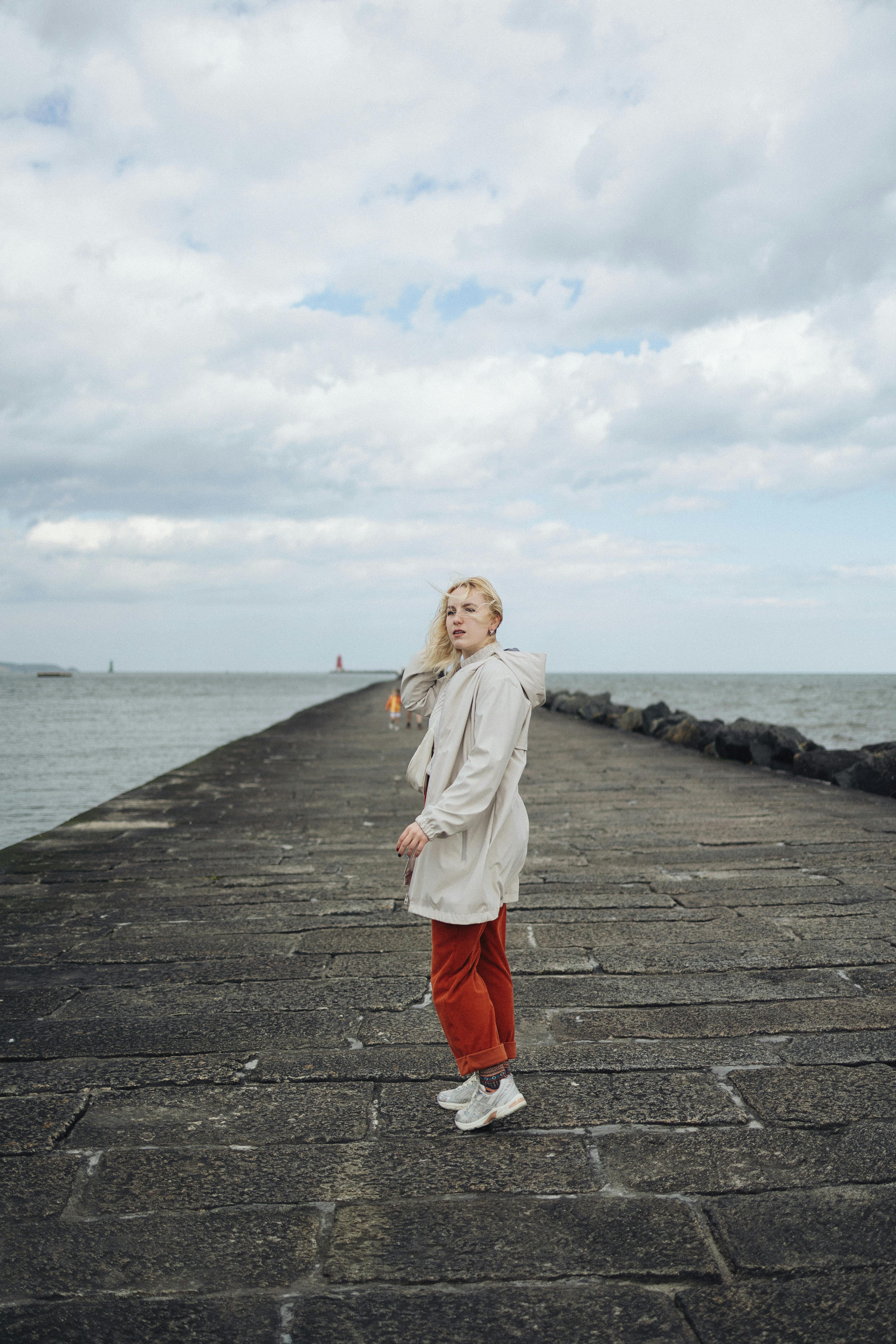 A woman stands on Poolbeg Pier, Dublin, with the sea and iconic lighthouse in the background.