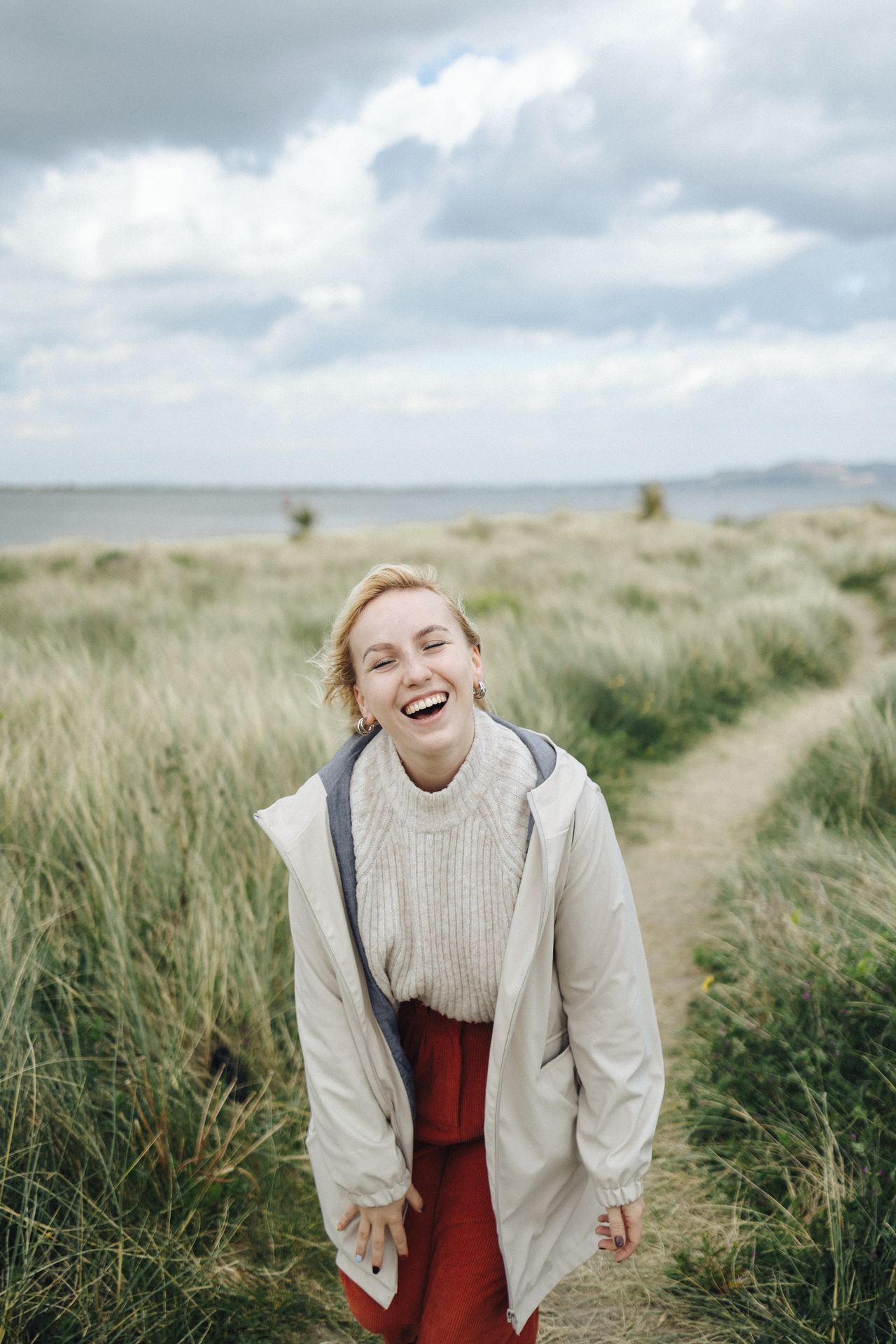 Laughing woman in a cream jacket and knit sweater on a grassland path