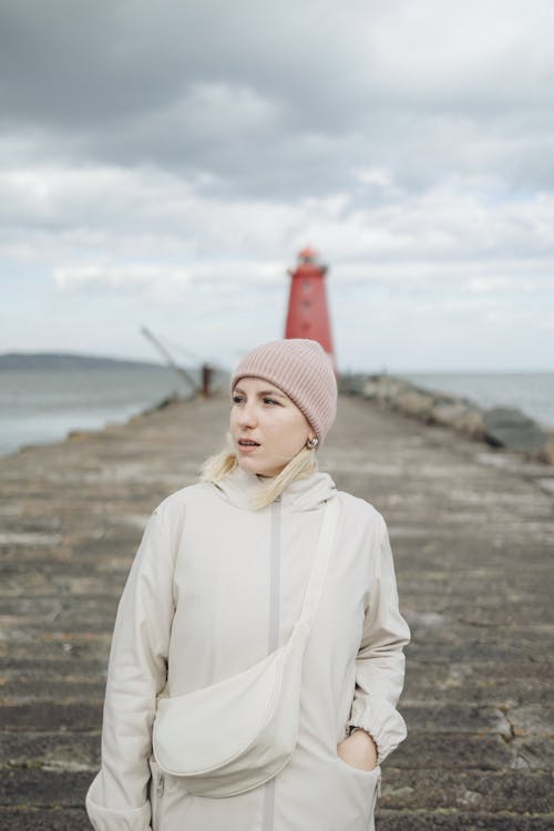A woman in a white coat and pink hat stands on a pier