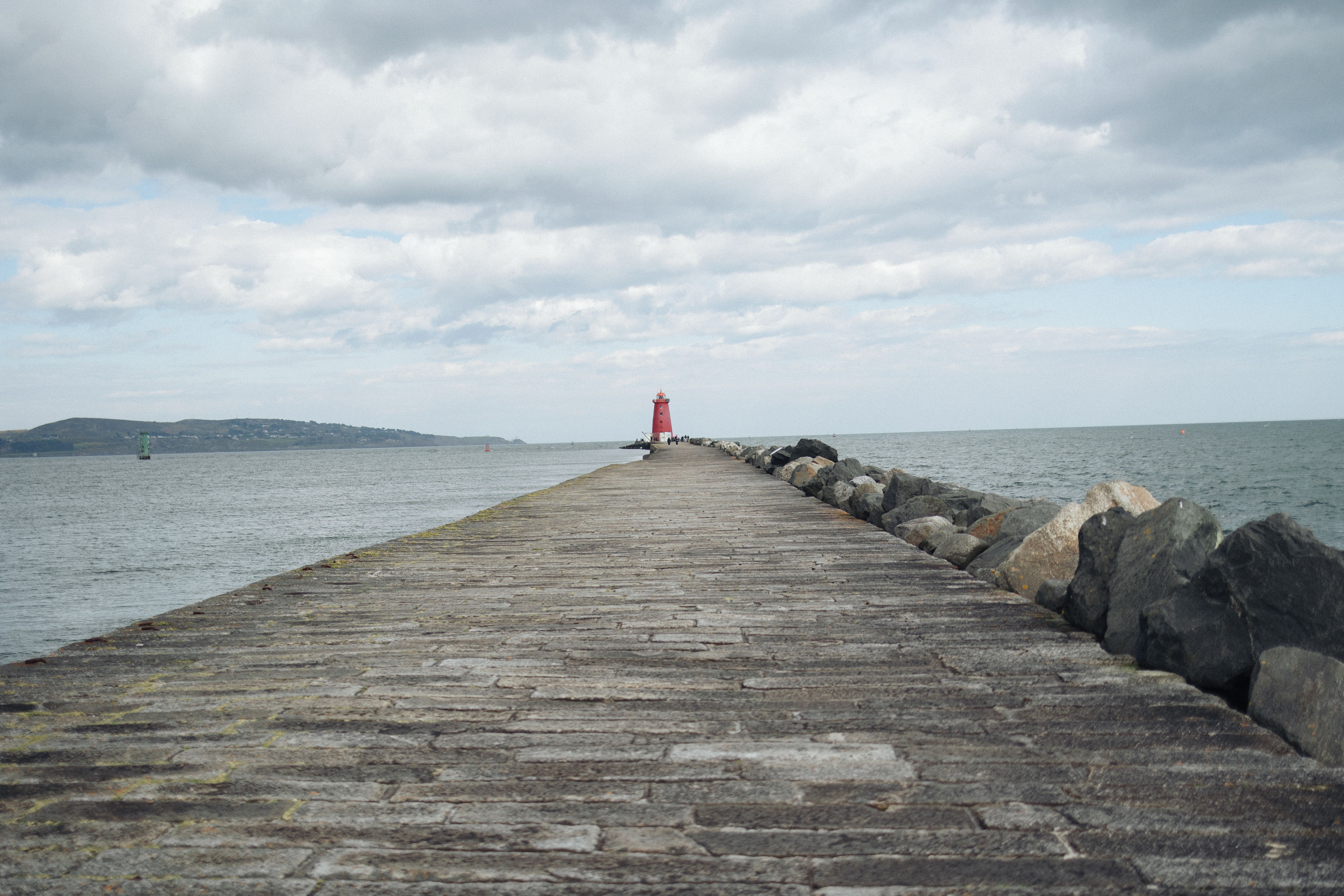 Scenic view of Poolbeg Lighthouse along the stone pier extending into the sea under cloudy skies.