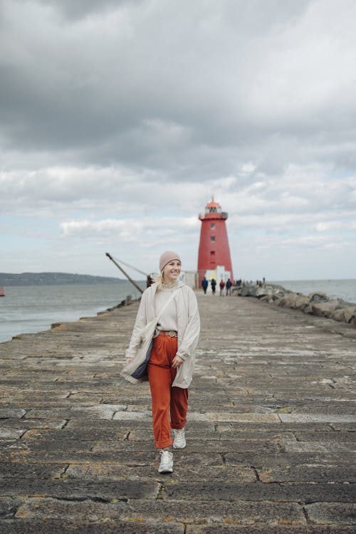 A woman walking on a pier with a red lighthouse in the background