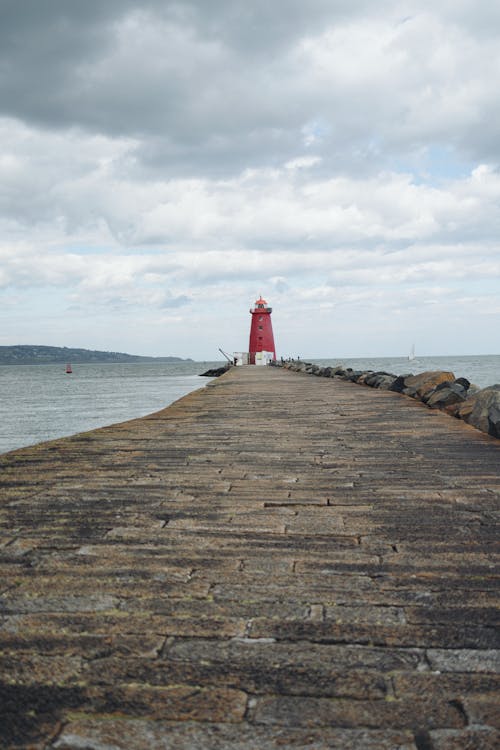 A red lighthouse on a pier with a cloudy sky
