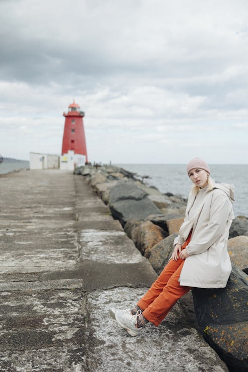 A woman sitting on a rock near a lighthouse