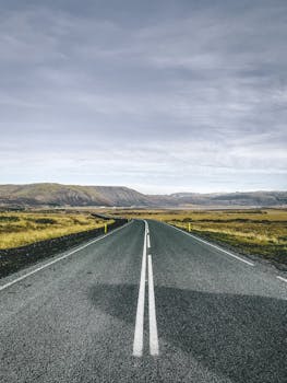 A straight road leading through the picturesque landscapes of Iceland's countryside under a cloudy sky.