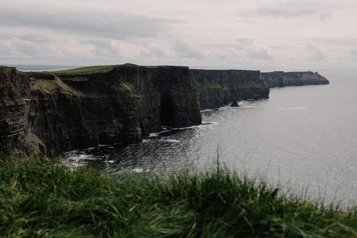 The Cliffs of Moher stretching along Ireland's Atlantic coast with green grass on top and crashing waves below