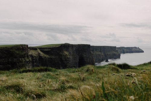 Free A dramatic view of the Cliffs of Moher with lush grass and a cloudy sky. Stock Photo