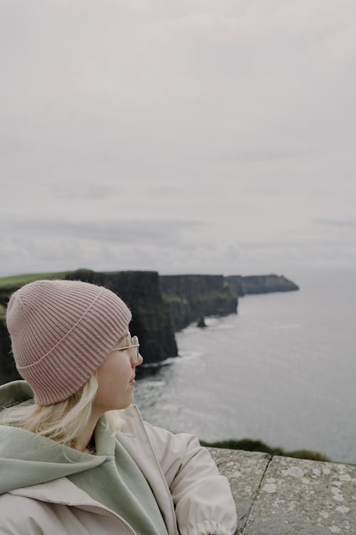 A woman wearing a pink beanie and glasses looking out to the ocean