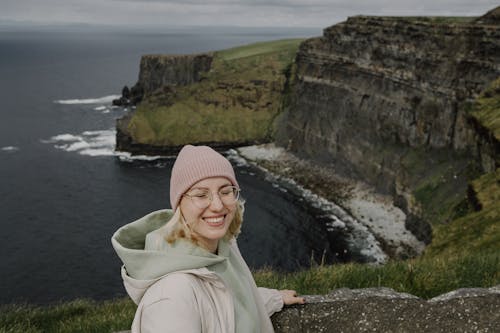 A woman in a pink hat and jacket standing on a cliff overlooking the ocean