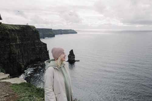 Free A woman stands smiling at the Cliffs of Moher, capturing serene coastal beauty. Stock Photo