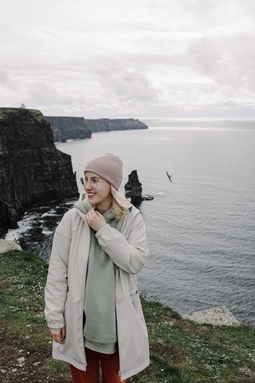 A woman in a pink coat and hat standing on a cliff