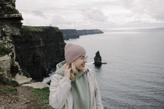 Smiling woman in a beanie enjoys the majestic Cliffs of Moher in cool weather.