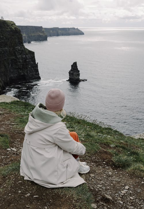 A woman sitting on a cliff overlooking the ocean