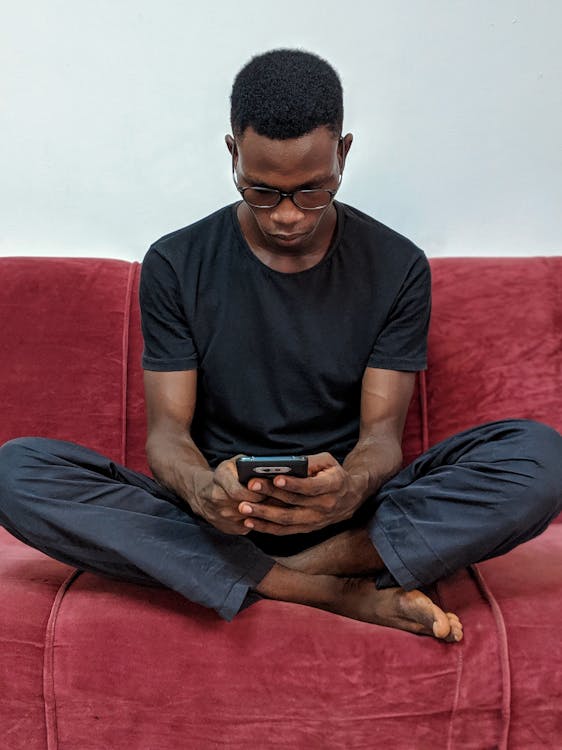 Man Sitting on Red Suede Sofa Holding Black Android Smartphone