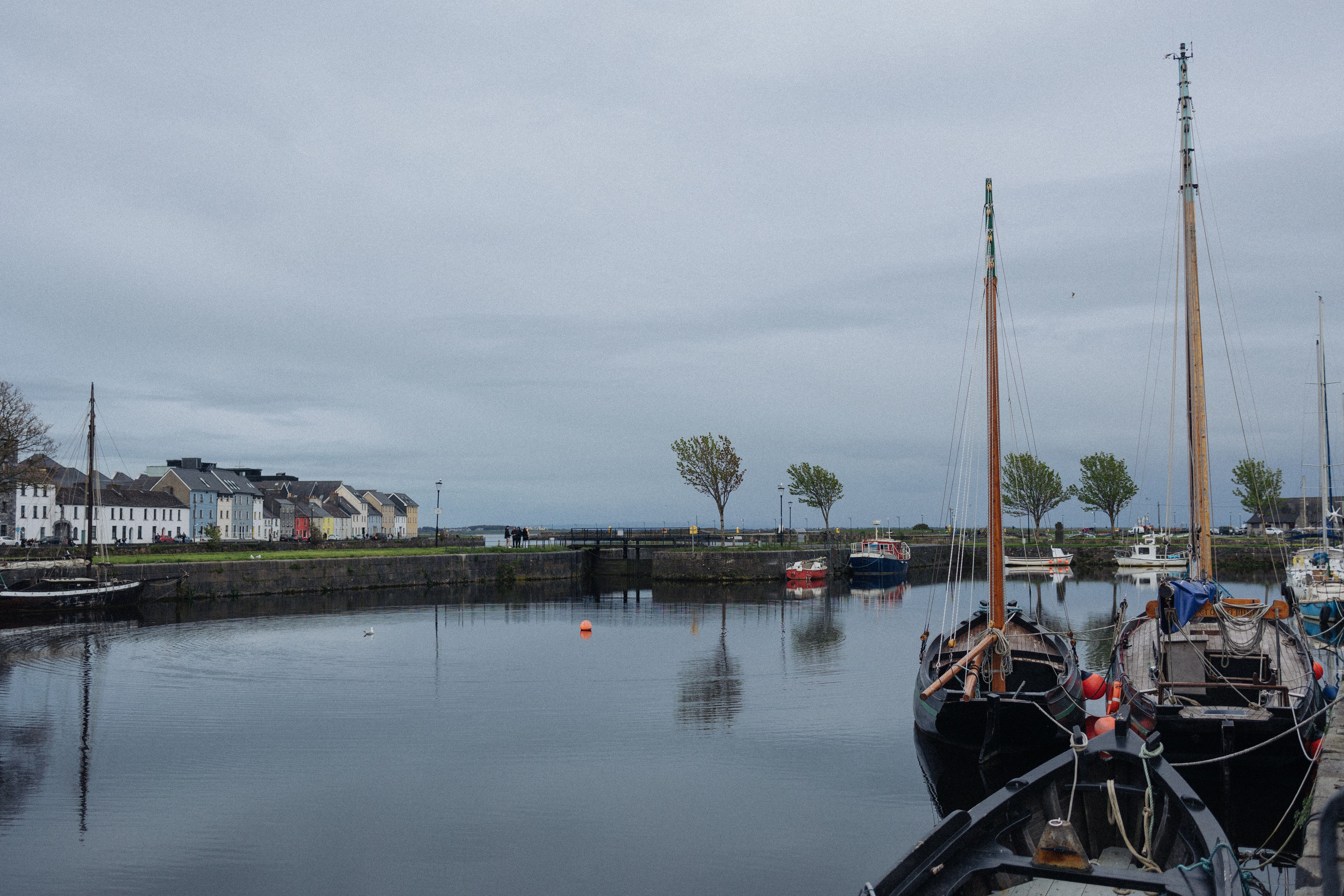 Tranquil canal scene with sailing boats and colorful buildings on a cloudy day, capturing serene waterfront charm.