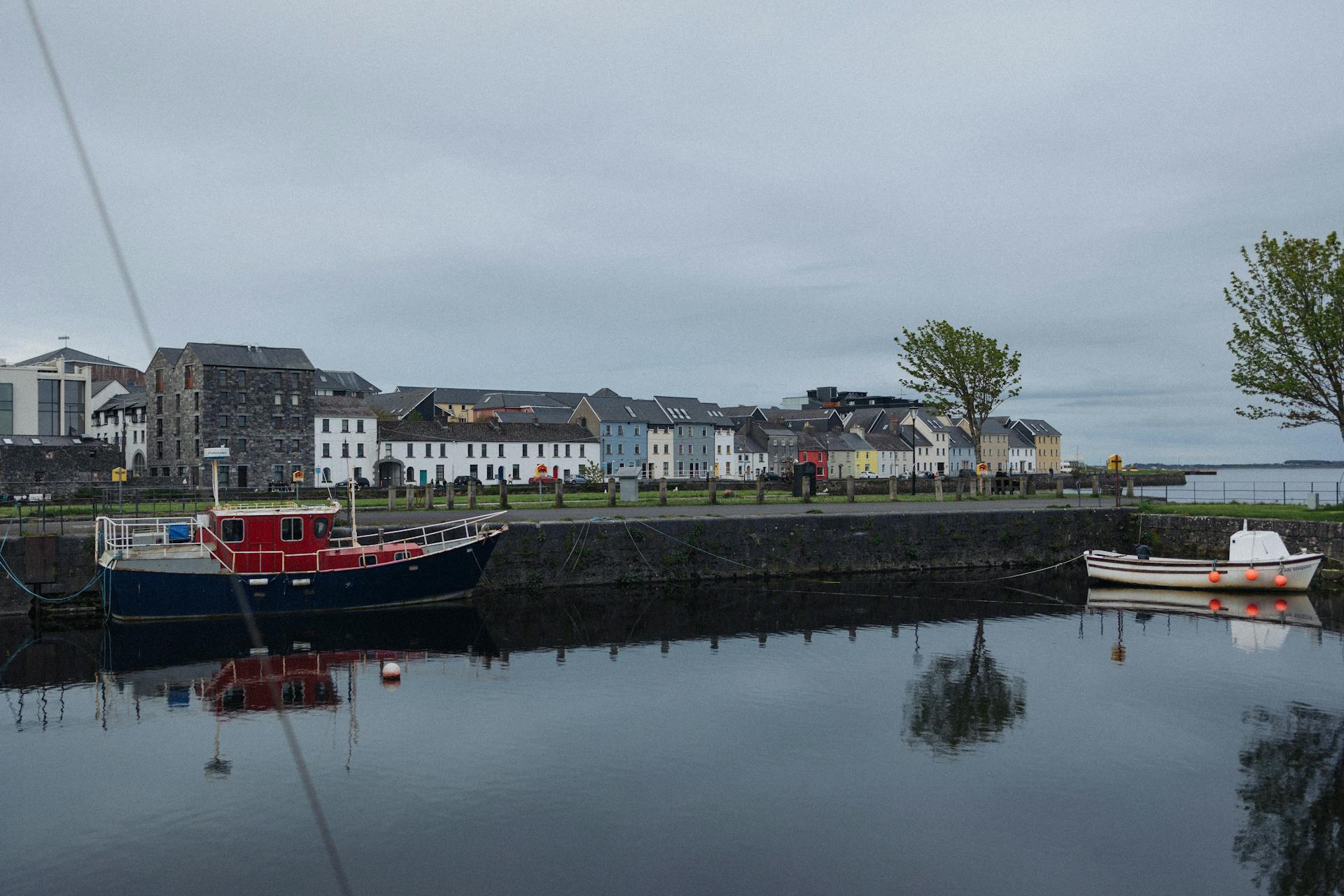 Scenic harbor with boats and vibrant buildings reflected in calm waters on a cloudy day.