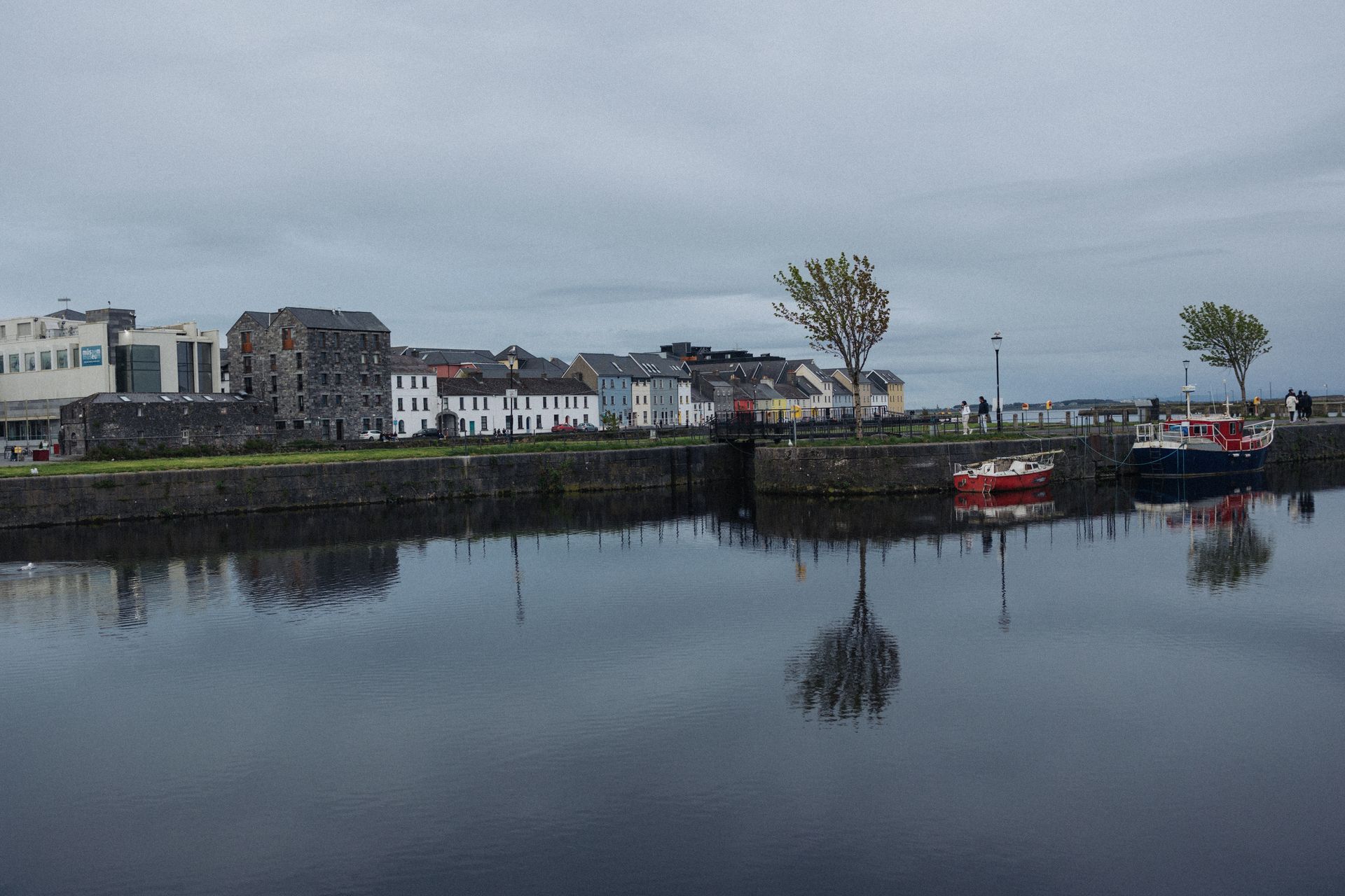 Serene harbor scene with colorful boats and historic buildings reflected in calm water.