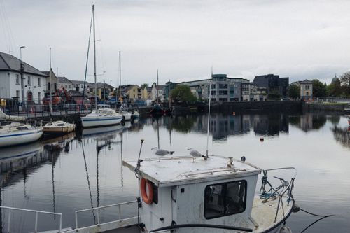 Free A tranquil urban harbor scene with boats, buildings, and reflections on a cloudy day. Stock Photo