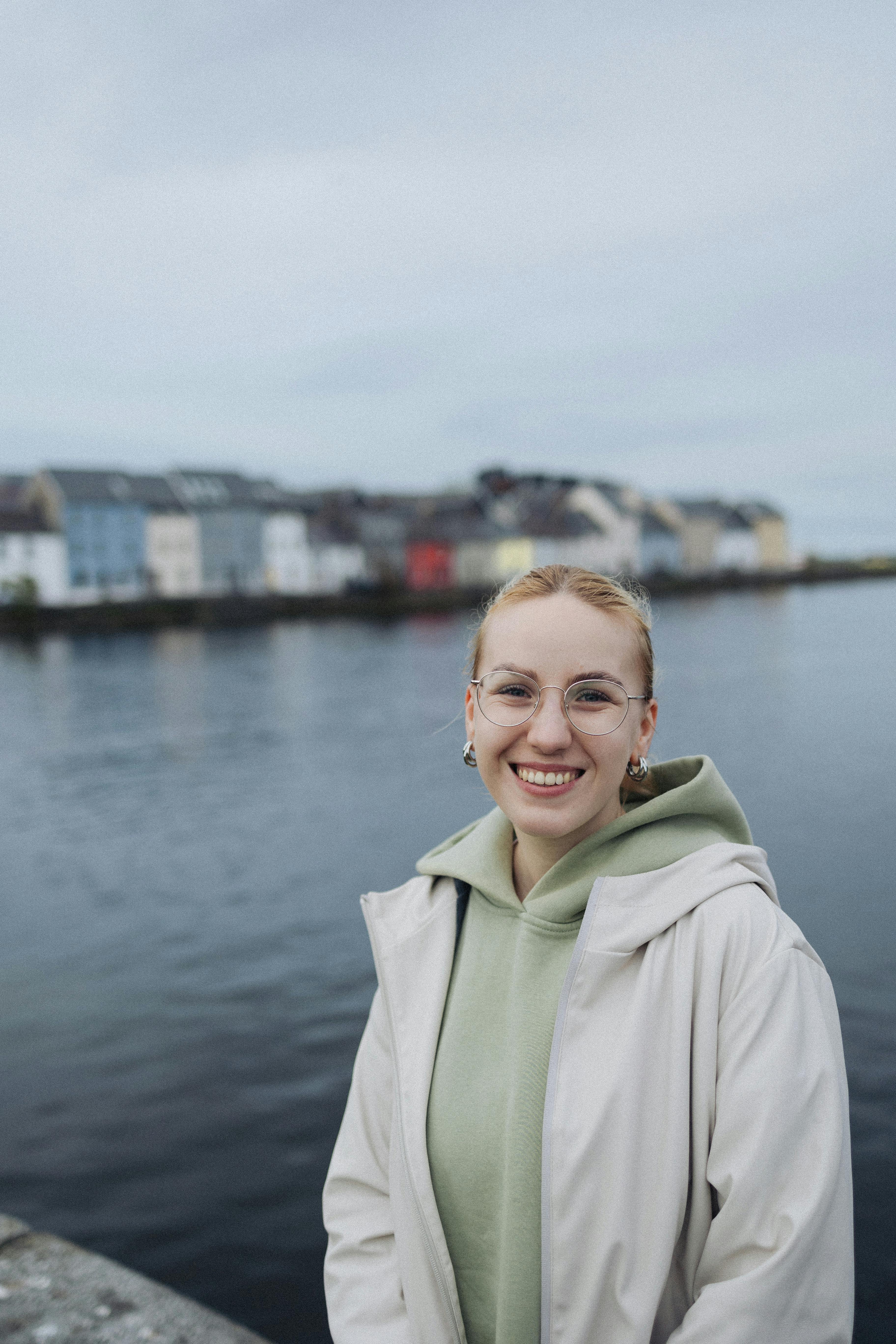 Happy woman in eyeglasses enjoying a day by the waterside with colorful buildings behind her.